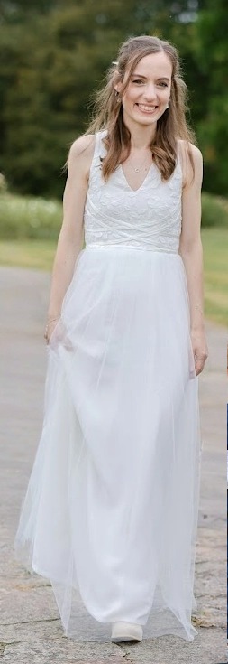 Alice portant sa robe de mariée faite main – décolleté V profond, broderies florales perlées et jupe tulle fluide – vue de face en extérieur